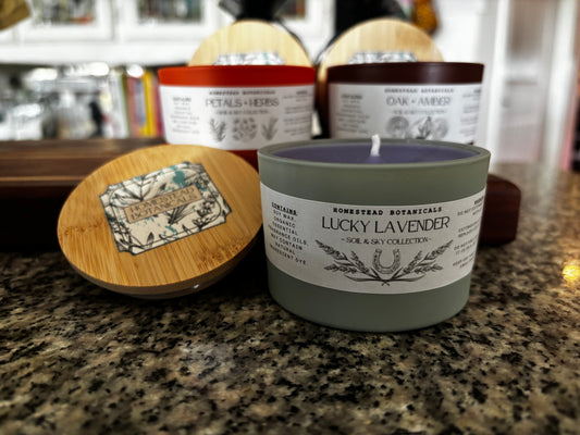 Homestead Botanicals Lucky Lavender candle on a countertop with other candles in the background.